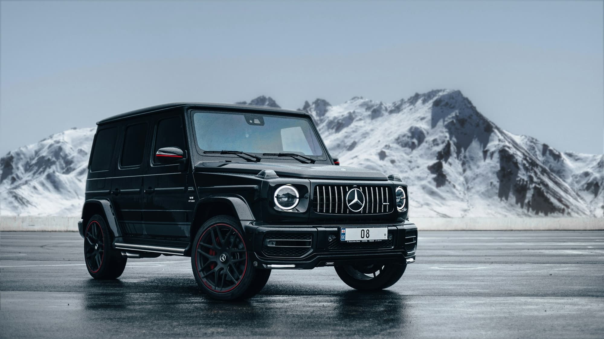 Black Mercedes-Benz G-Class SUV on a wet road in front of snowy mountains